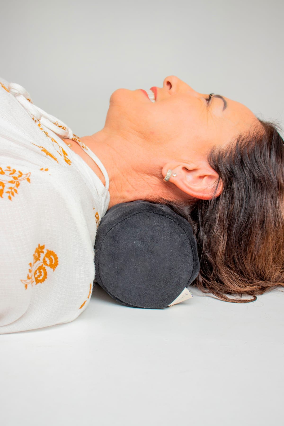Silvana deitada com o pescoço apoiado em um rolo cervical magnético